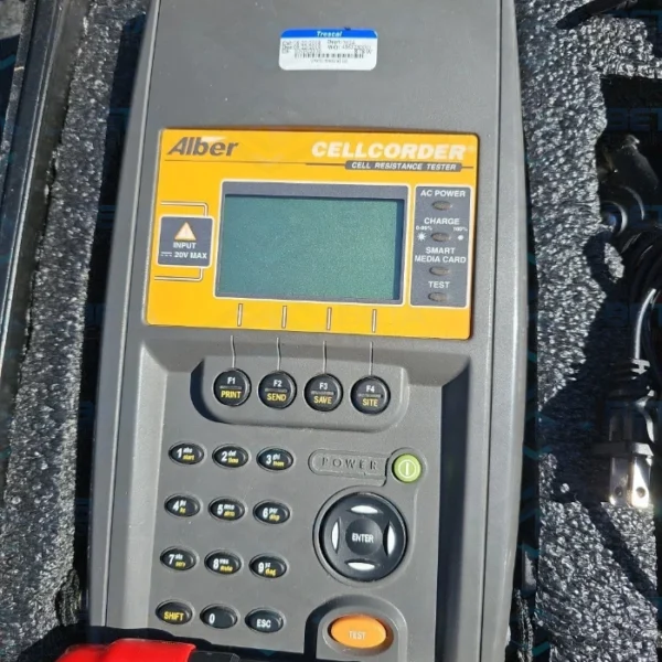 Close-up top-down view of the front control panel of an Alber Cellcorder CRT-300 Cell Resistance Tester resting inside custom foam padding. The grey and yellow handheld unit features a central graphic LCD screen, LED operational status indicators for AC power, charge, and smart media card test functions, a Trescal calibration sticker on the top housing, function keys (F1 to F4), a full numeric and alphanumeric keypad, directional navigation buttons with a central ENTER key, and an orange test button.