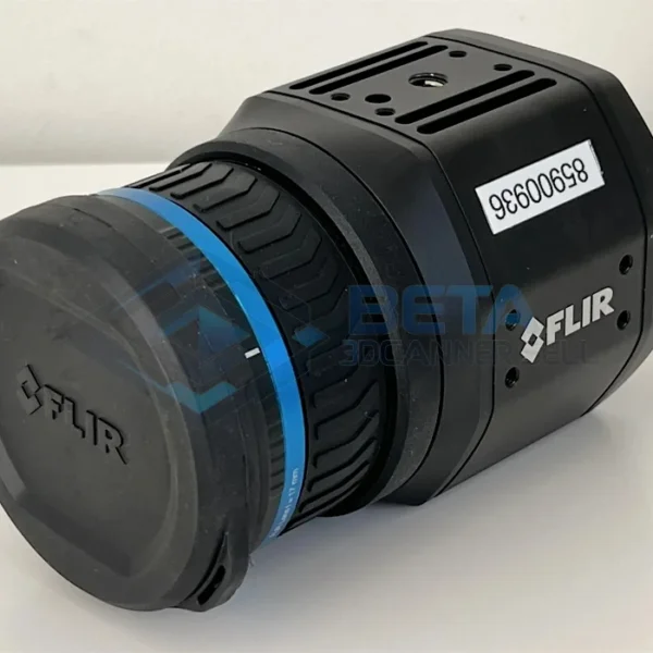 FLIR A700 A close-up, angled view of a black FLIR thermal imaging camera. The front features a lens protected by a lens cap that has the FLIR logo embossed on it. A textured blue rubber focus ring with a chevron pattern is prominent around the lens barrel. The main camera body displays the white FLIR logo and an inventory label sticker with the number "85900936" printed on it. Multiple mounting points and screws are visible on the top and side of the rugged body. The camera is resting on a clean white table surface.