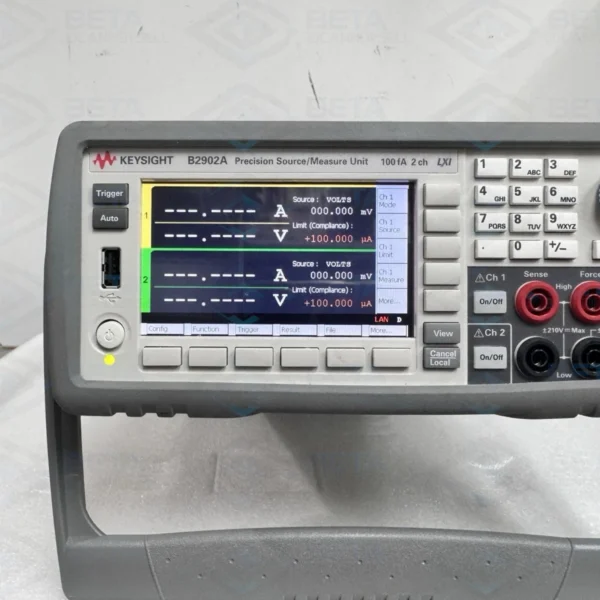 Front panel close-up view of a Keysight Agilent B2902A 2-Channel Precision Source/Measure Unit powered on against a studio background. The 4.3-inch color LCD display shows active voltage sourcing and compliance current limit settings for Channel 1 and Channel 2. The front control interface features softkey menu buttons, a full numeric keypad, Channel 1 and Channel 2 input/output banana jack terminals, a front USB port, and an illuminated power button.