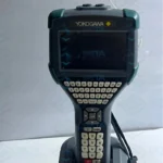 Front view of the Yokogawa YHC5150X-01 FieldMate Handheld Communicator sitting in its charging cradle. The device features a rugged grey industrial casing with green rubber corner bumpers, a yellow-and-black Yokogawa logo above a large display screen, a full QWERTY keyboard with white tactile buttons, directional navigation pad, and a numeric keypad at the bottom.